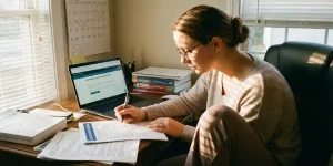 Verpleegkundige studeert aan houten bureau met laptop, kalender en certificeringsdocumenten in warm daglicht